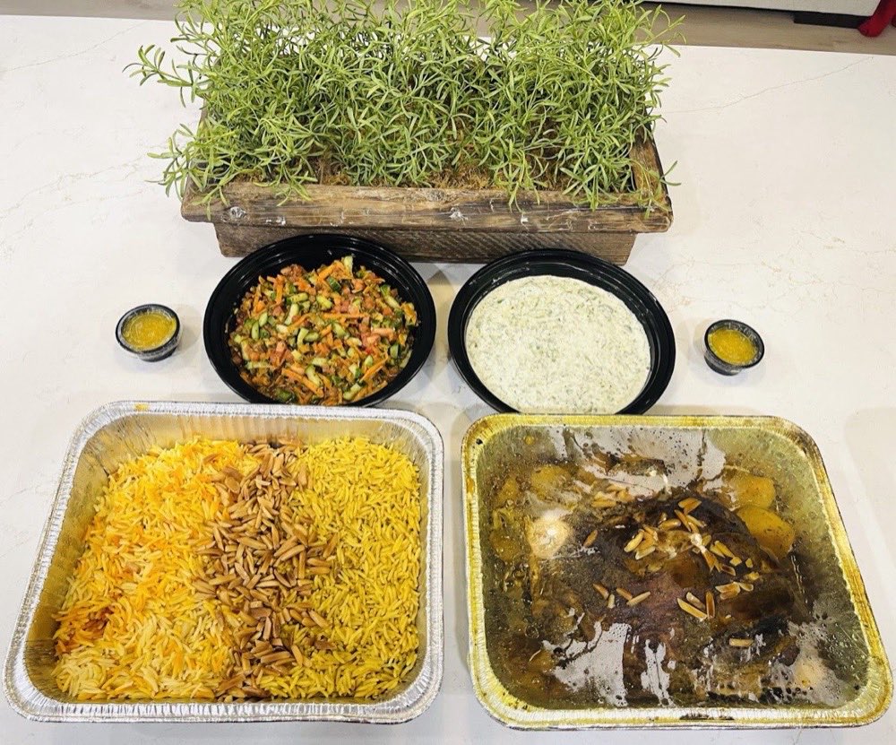 Catering trays of saffron rice and slow-cooked lamb laid out with salads.